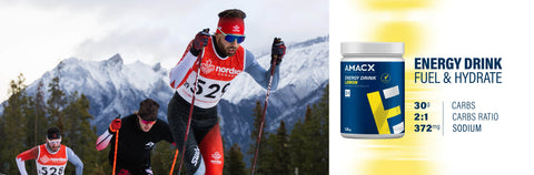 Cross-country skiers with a focus on an AMACX energy drink container against a mountainous background.